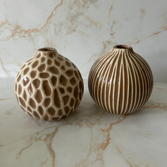Stijlvolle set van twee keramieken vaasjes in warme beige- en bruintinten. Elk vaasje heeft een uniek reliëfpatroon: één met een speels organisch motief en één met een elegant verticaal ribpatroon. Samen vormen ze een rustige maar luxe uitstraling.
